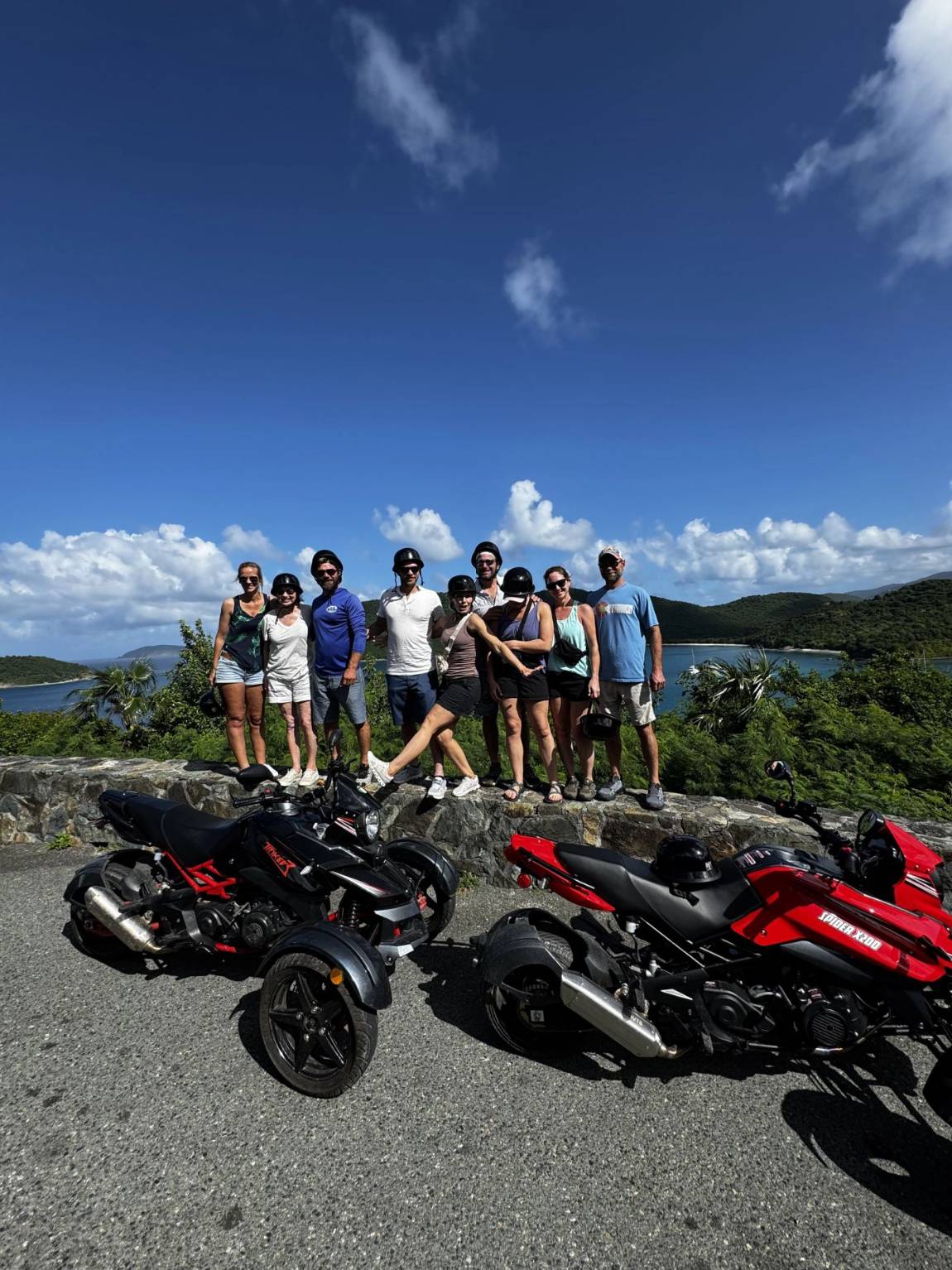 A group of nine guests posing with three-wheel trikes on a sunny St. John day
