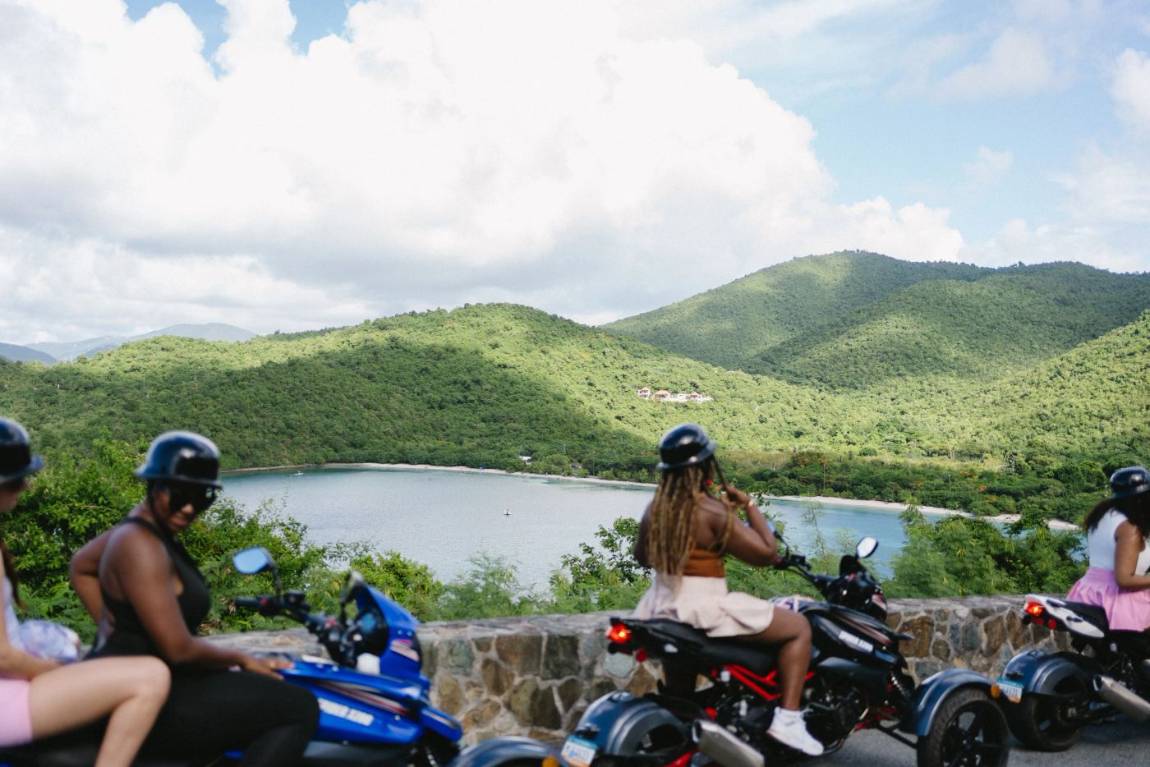 Riders in helmets pausing at an overlook above a St. John bay