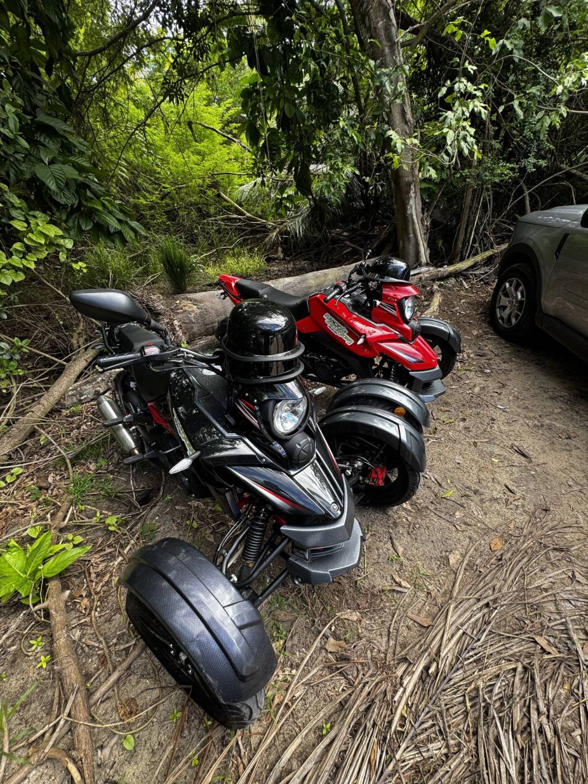 Red and black three-wheel trikes parked in the shade