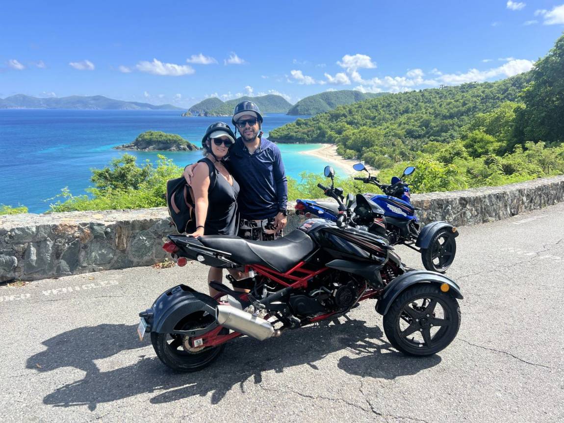 A couple posing with three-wheel trikes along the St. John coastline